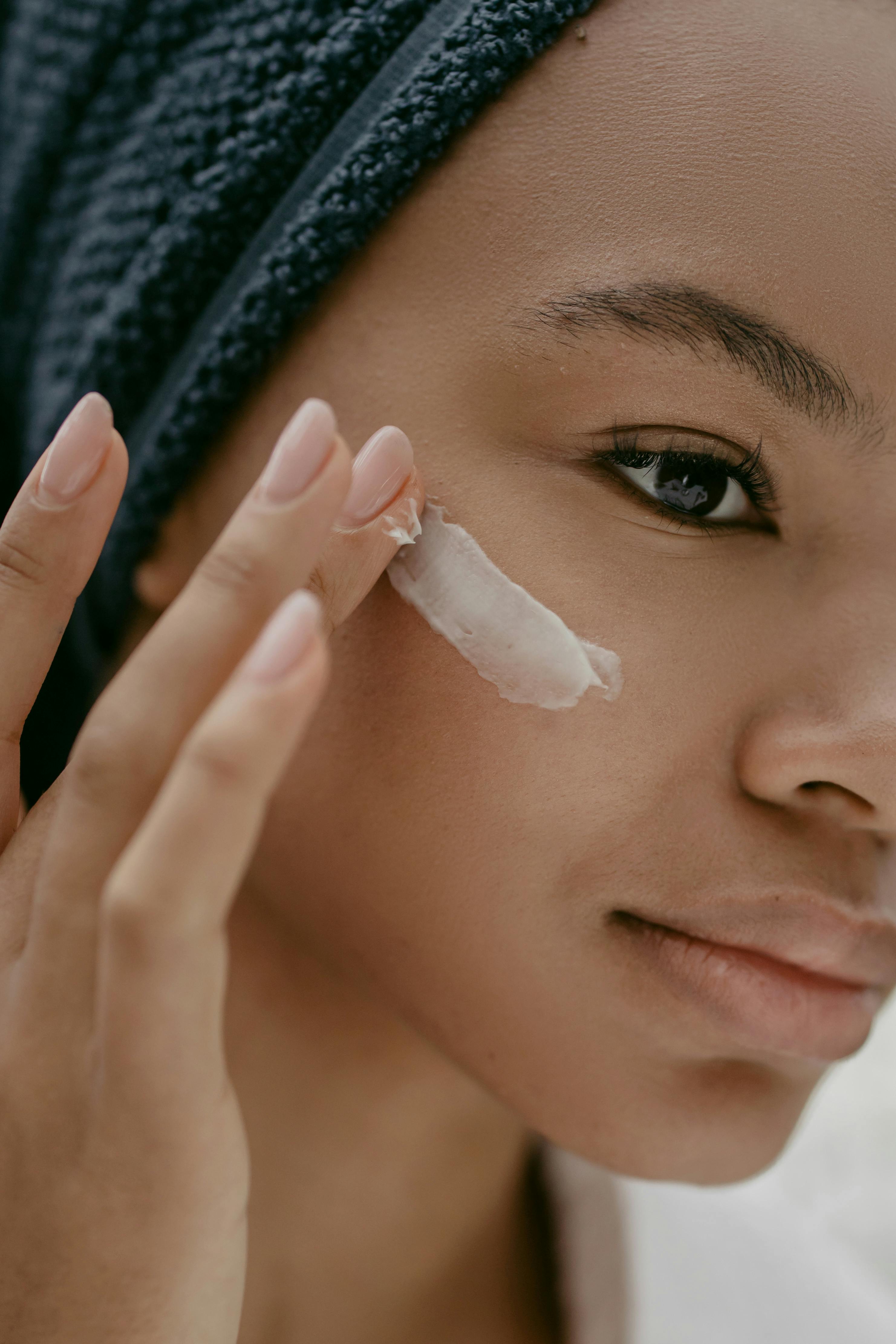 Woman applying cream to her face with a towel on her head